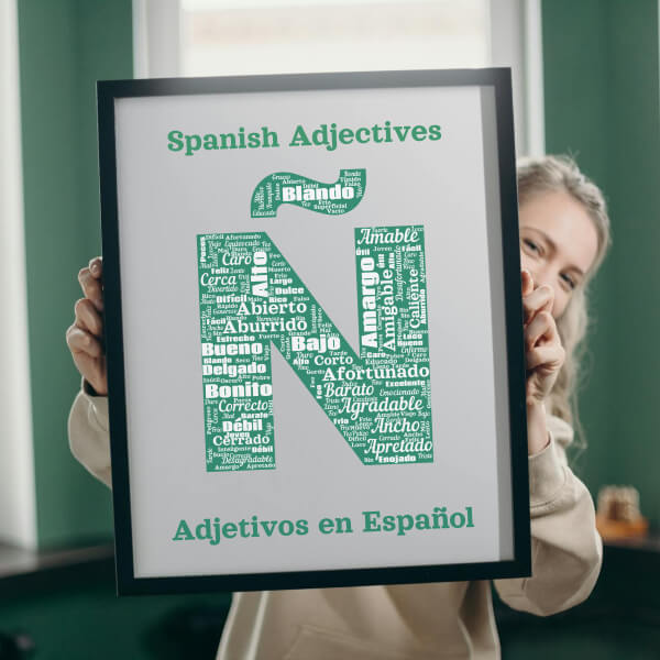 A teacher holding up a poster featuring a word cloud of Spanish adjectives shaped like the letter Ñ. Adjectives include 'Abierto', 'Importante', and 'Peligroso'.